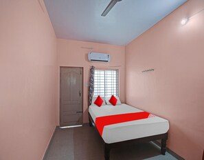 A bedroom with a bed, a window with curtains, an air conditioning unit, and a door.