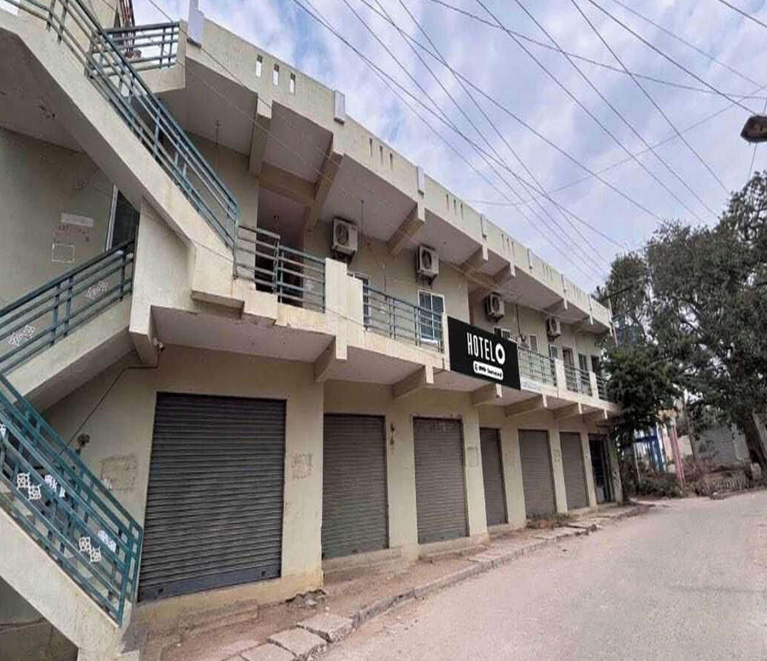 A multi-story hotel with a sign indicating it is a hotel. There are balconies on the upper floors, and the ground floor has closed shutters.