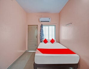 A room with a bed, a window with curtains, an air conditioning unit, and a door.