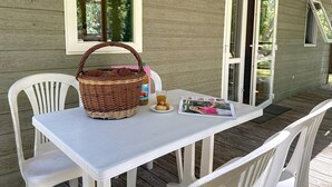 Un área de estar al aire libre techada con una mesa, sillas, una cesta, una botella y una revista.