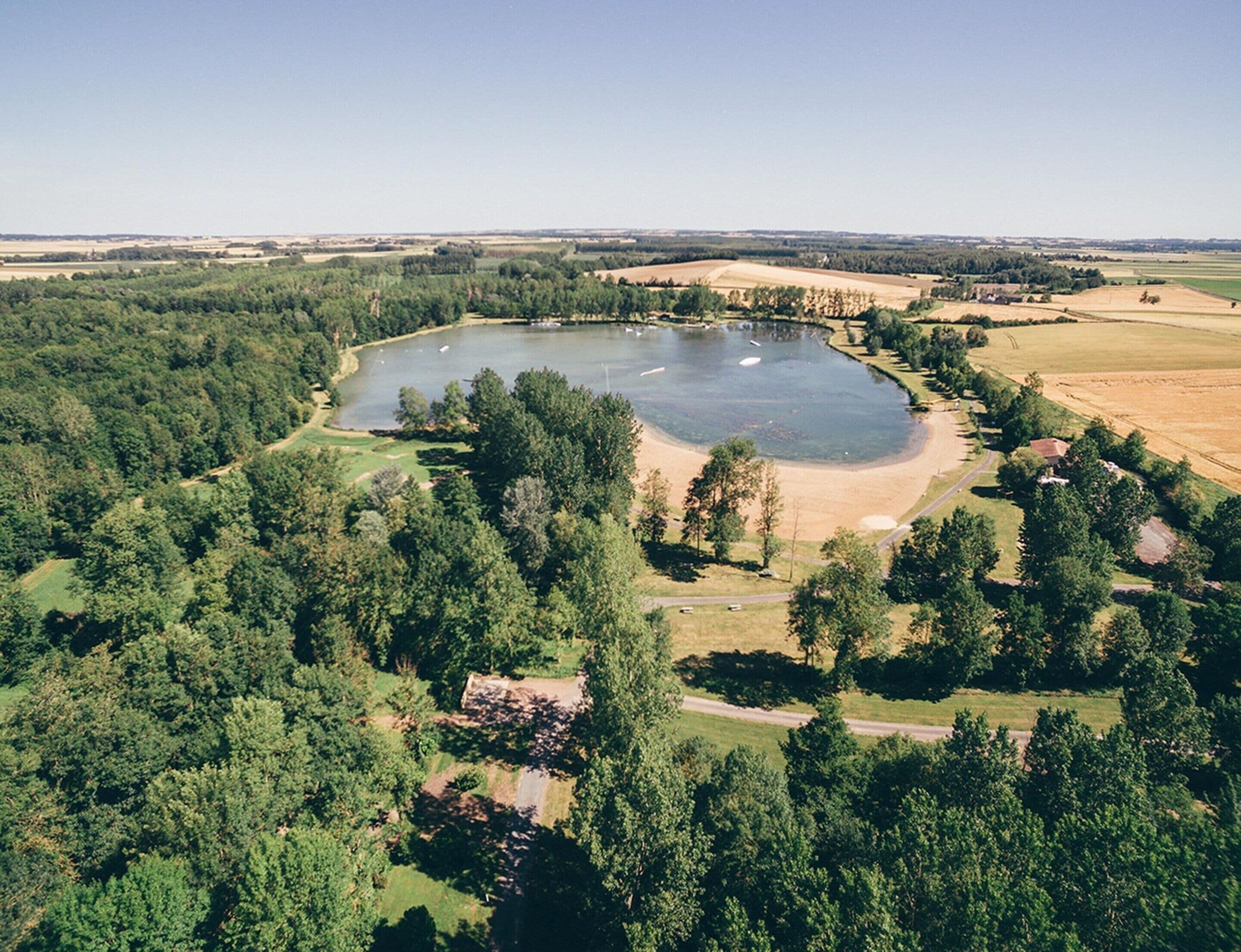 An aerial view of a lake surrounded by dense forest and open fields.