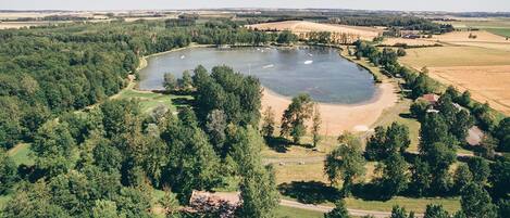 An aerial view of a lake surrounded by dense forest and open fields.