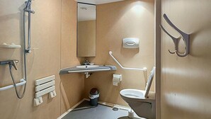 Un baño con ducha, lavabo, inodoro y barras de apoyo.