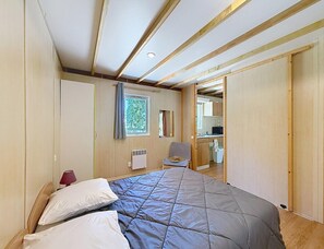 A bedroom with a bed, a chair, a radiator, and a window. - Lakeside 2BR Chalet for Four (Moncontour)