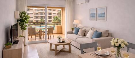 A modern living room with a sofa, a coffee table, a TV, and a dining area with a table set for two.