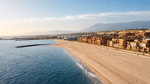 A coastal cityscape with a beach, buildings, and mountains in the background.