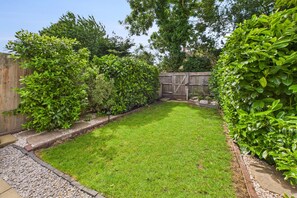 Un jardin bien entretenu, avec une pelouse verdoyante, une clôture en bois et divers arbustes.