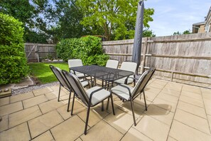 Une terrasse extérieure avec une table et des chaises, entourée d’une clôture en bois et de verdure.