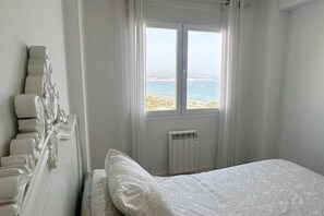 A bedroom with a bed, a radiator, and a window with a view of the sea.