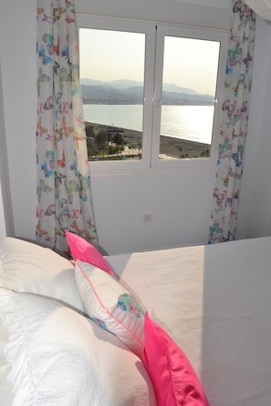 A bedroom with a bed, a window with curtains, and a view of a body of water and mountains. - Piso del Mar. Stunning views just 50 meters from the beach (Torre del Mar)