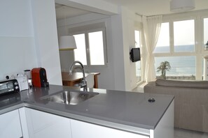 A modern kitchen with a built-in sink, a dining area with a table and chairs, and a view of the sea through large windows.