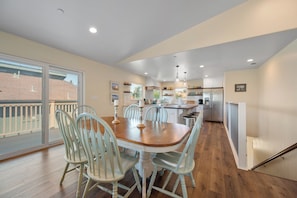 A spacious dining area with a wooden table and chairs, a kitchen in the background, and a view through a sliding glass door. - The Otter House on Happy Hill! Ocean Views & Short Walk to Moonstone Beach! (CAMBRIA)