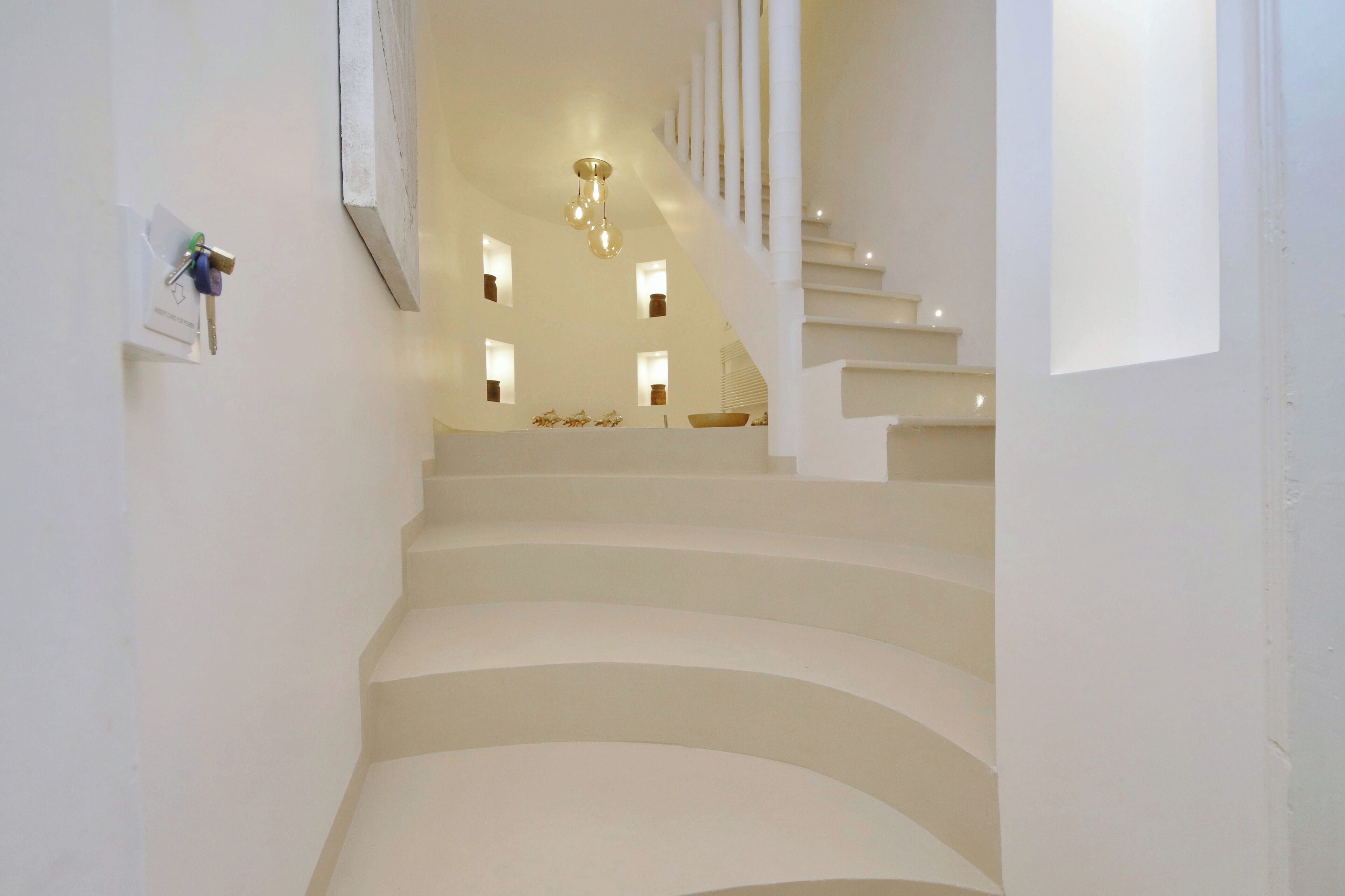 A staircase with a modern design, leading to a landing with a chandelier and small windows.