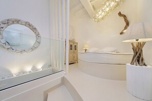 A modern bedroom with a curved bed, a round mirror, a bedside lamp, and a decorative wooden piece. - Vrbo Property (Roma)