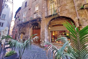 A narrow cobblestone street with a building featuring a wooden door, balconies with plants, and a shop with glass display. - Vrbo Property (Roma)