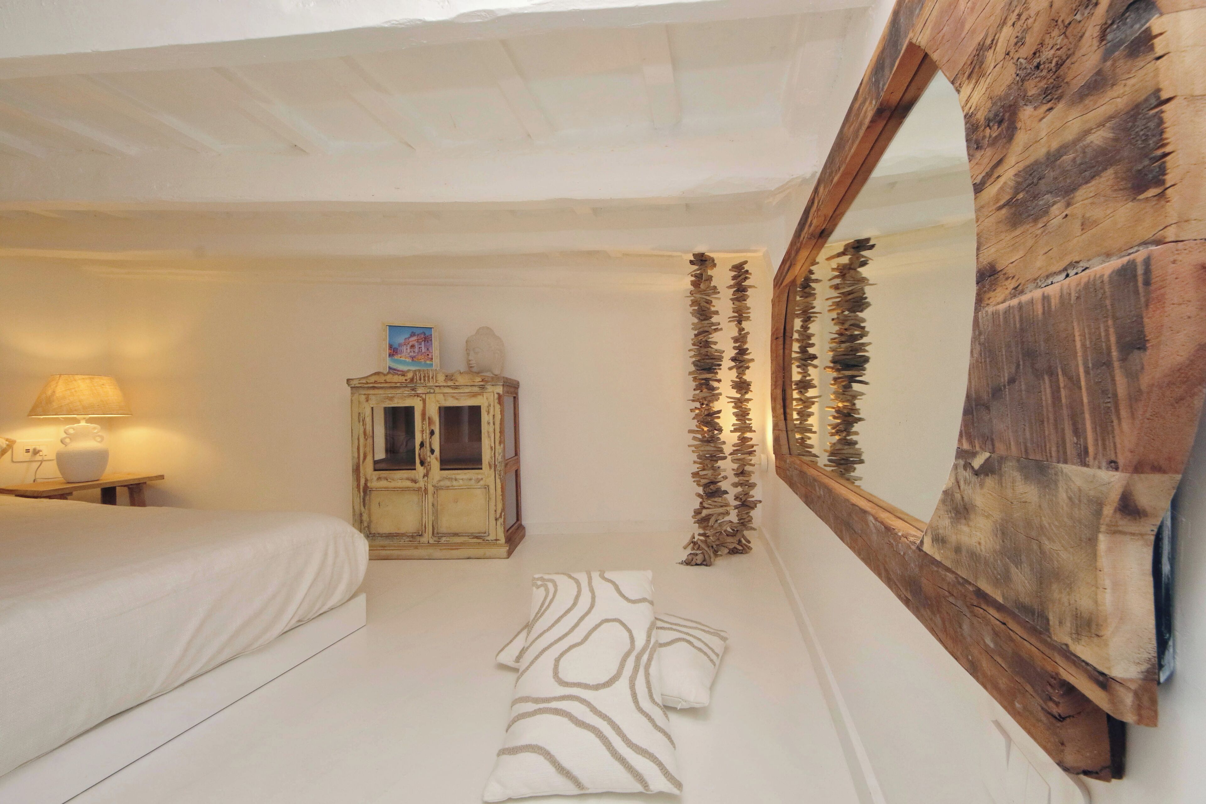 A bedroom with a bed, a wooden cabinet, a mirror, and a wall-mounted wooden shelf.