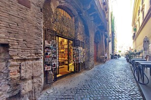 A narrow cobblestone street with a bookstore on the left and a row of outdoor seating on the right. - Vrbo Property (Roma)