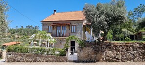 A stone house with a tiled roof, a balcony, and a garden with potted plants.