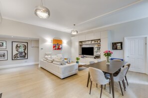 Ein modernes Wohnzimmer mit einem weißen Sofa, einem Esstisch mit Stühlen und einem an der Wand befestigten Flachbildfernseher.