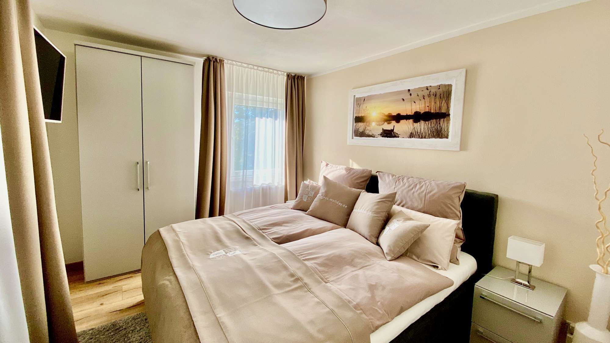 A hotel room with a bed, a nightstand, a lamp, a wardrobe, and a painting on the wall.