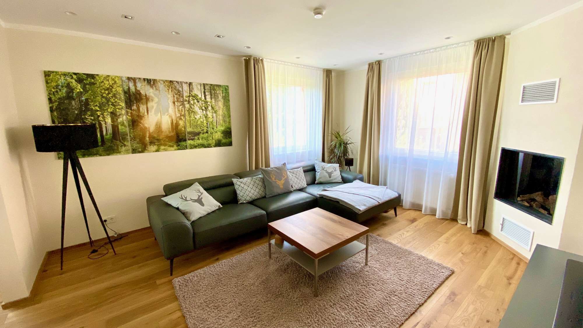 A modern living room with a sectional sofa, a coffee table, a painting of a forest, and a fireplace.
