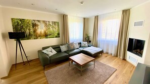 Ein modernes Wohnzimmer mit einem Ecksofa, einem Couchtisch, einem Waldgemälde und einem Kamin.