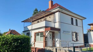 Ein zweistöckiges Gebäude mit flachem Dach, einem gut sichtbaren Eingang und einem Schild, das es als Ferienhaus kennzeichnet.