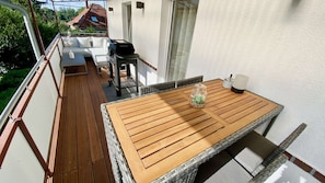 Ein Balkon mit Holztisch, Grill und Korbstuhl.