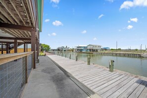 A wooden pier leading to a waterfront property with a covered area and a view of houses across the water. - SeaGlass Smiles | Canal-Front, Private Dock & Dog-Friendly (Rockport)