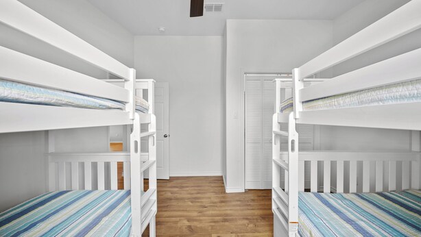 A room with bunk beds, wooden flooring, and a white door. - SeaGlass Smiles | Canal-Front, Private Dock & Dog-Friendly (Rockport)