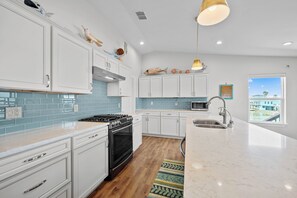 A modern kitchen with white cabinets, a black stove, and a view of a coastal area. - Fall Special! Buy 2 nights, get your 3rd night Free! At Seaglass Smiles (Rockport)