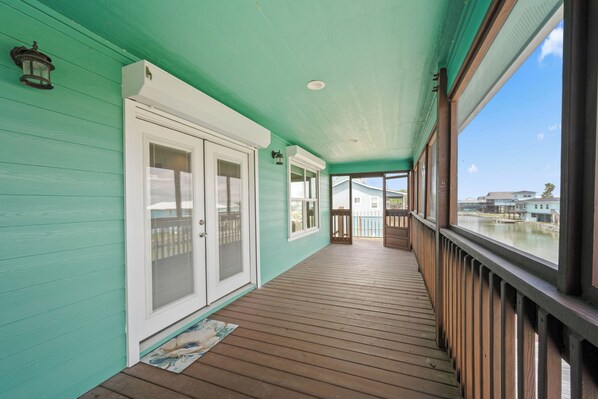 A covered wooden deck with a view of a body of water and buildings in the background. - Fall Special! Buy 2 nights, get your 3rd night Free! At Seaglass Smiles (Rockport)