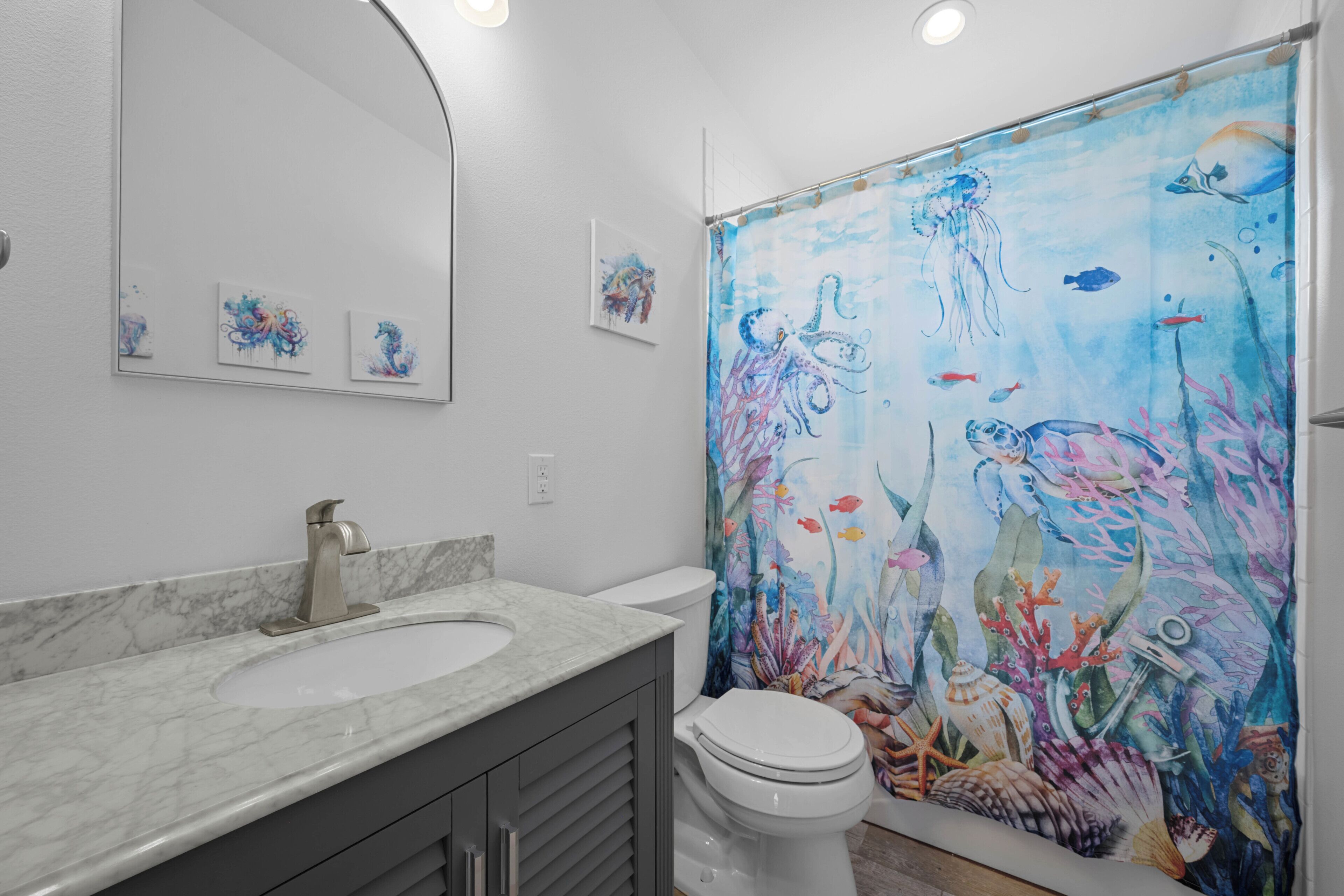 Une salle de bain avec un grand rideau de douche représentant des scènes sous-marines, un lavabo en marbre et des toilettes.