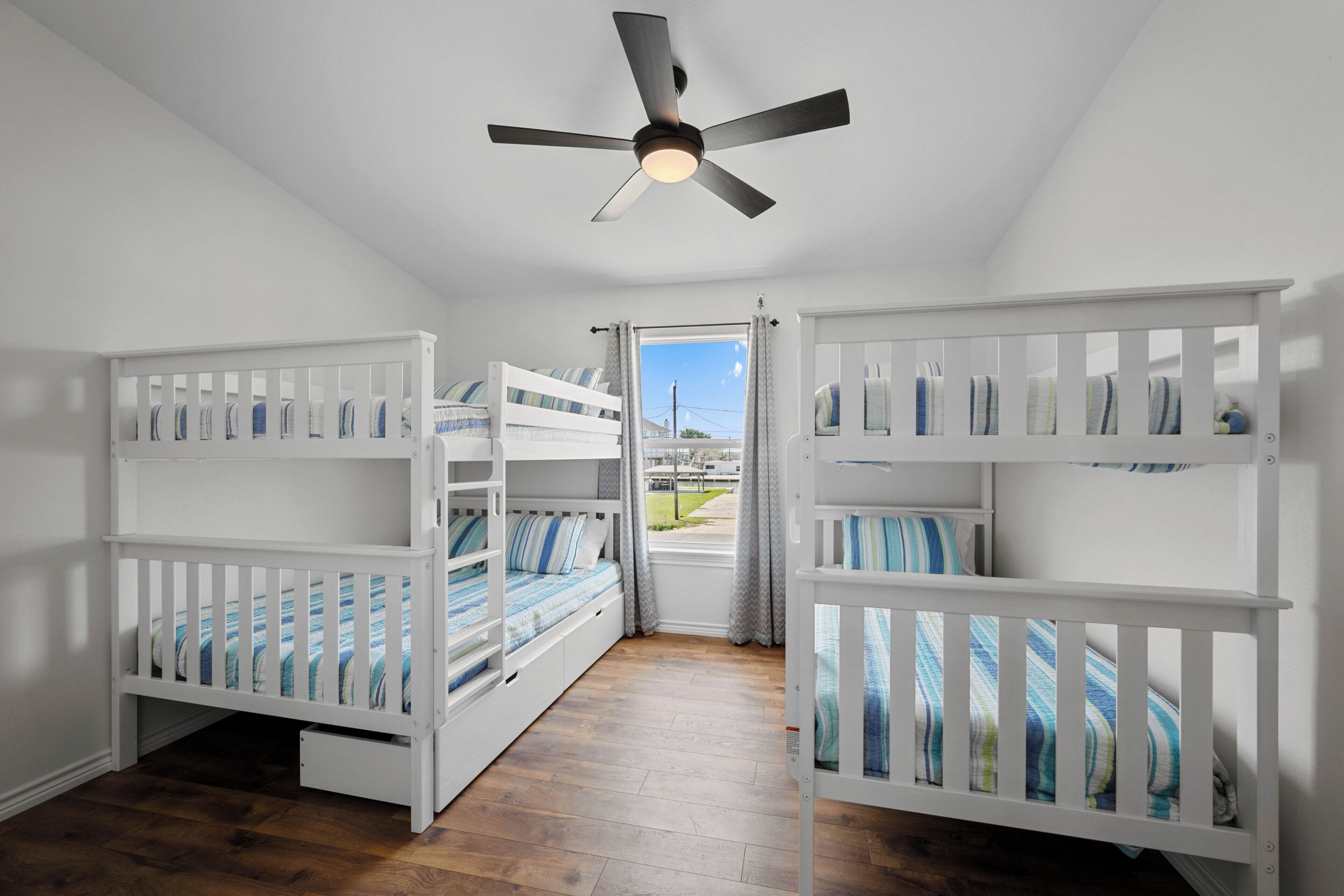 Une chambre avec deux lits superposés, un ventilateur de plafond et une fenêtre avec des rideaux.