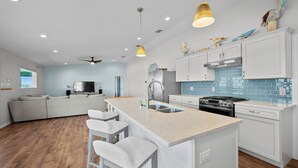 A modern kitchen with a central island, stainless steel appliances, and a blue-tiled backsplash. - SeaGlass Smiles | Canal-Front, Private Dock & Dog-Friendly (Rockport)