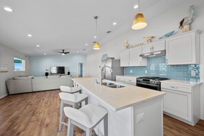 A modern kitchen with a central island, stainless steel appliances, and a blue-tiled backsplash. - SeaGlass Smiles | Canal-Front, Private Dock & Dog-Friendly (Rockport)