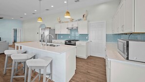 A modern kitchen with white cabinetry, a central island with bar stools, a stove, and a microwave. - SeaGlass Smiles | Canal-Front, Private Dock & Dog-Friendly (Rockport)