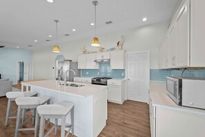 A modern kitchen with white cabinetry, a central island with bar stools, a stove, and a microwave. - SeaGlass Smiles | Canal-Front, Private Dock & Dog-Friendly (Rockport)