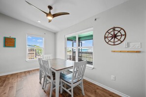 A dining area with a wooden table and chairs, a ceiling fan, and a view through large windows. - Fall Special! Buy 2 nights, get your 3rd night Free! At Seaglass Smiles (Rockport)