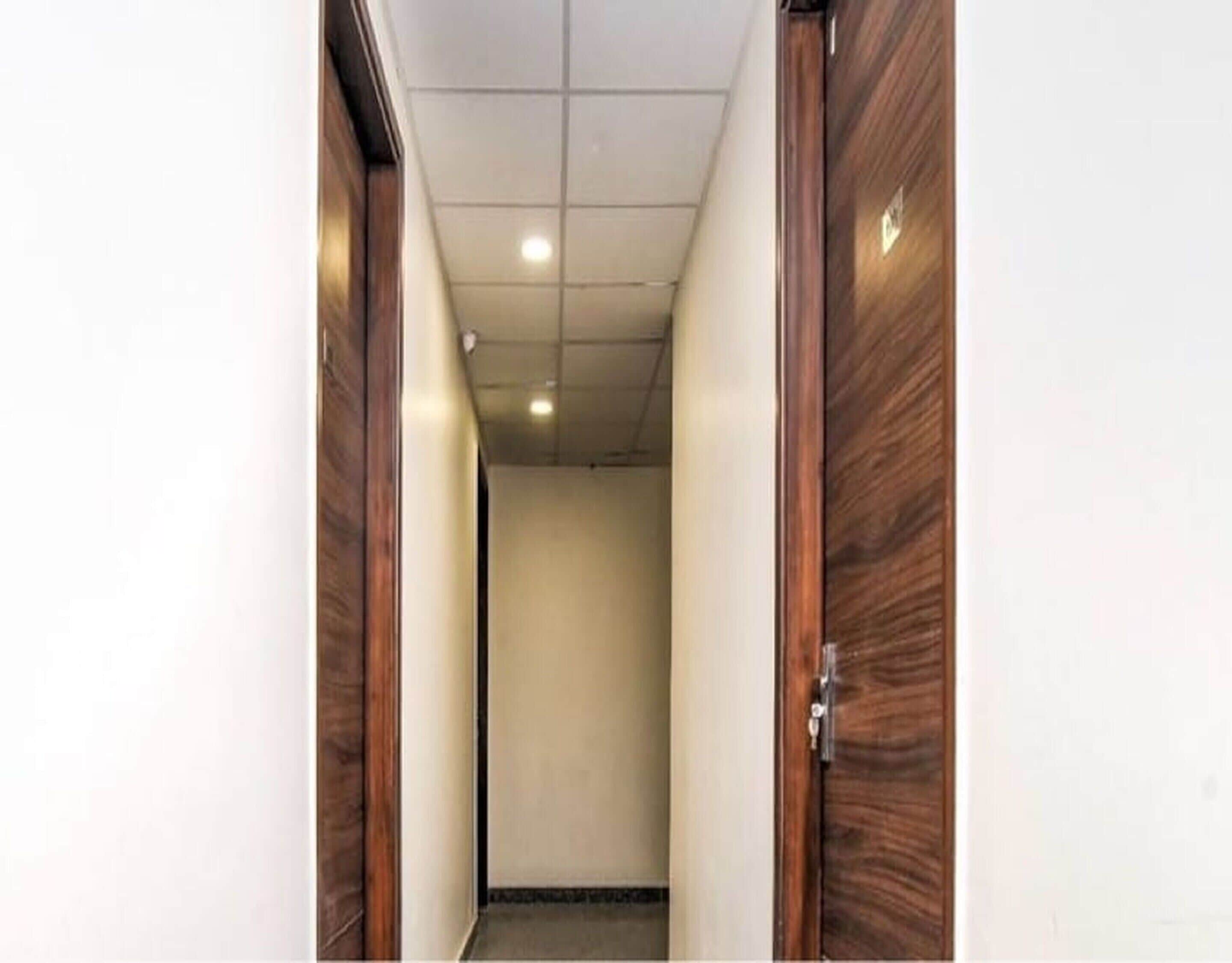 A narrow hallway with wooden doors on either side, a tiled ceiling, and a plain wall.