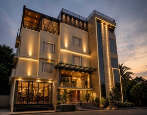 A multi-story hotel with a modern design, featuring balconies, large windows, and a well-lit entrance. - Deluxe Room sn Bliss Premium Ladies pg (Bengaluru)