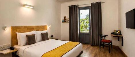 Habitación de hotel con cama, escritorio, silla, televisor y ventana con cortinas.