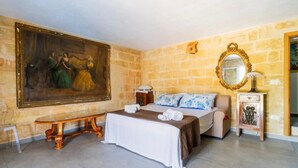 A hotel room with a large painting, a bed with a blue floral bedspread, a bench, and a wooden nightstand with a lamp. - Elegant 19th-century farmhouse located 700 meters from Baia Verde, Gallipoli (Gallipoli)