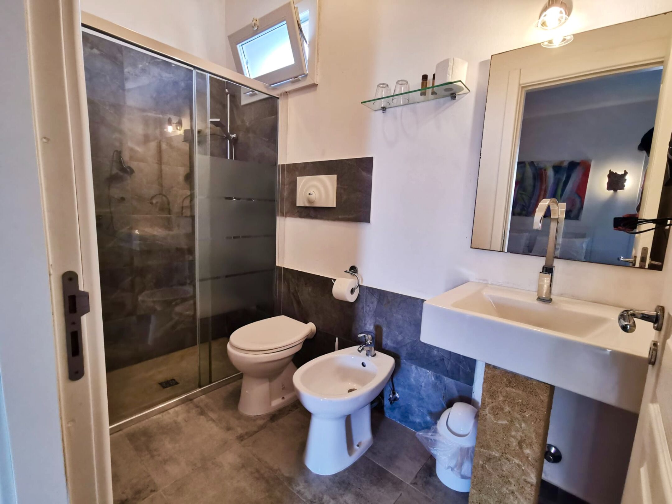 Ein Badezimmer mit Duschkabine aus Glas, Toilette, Bidet und Waschbecken mit Spiegel.