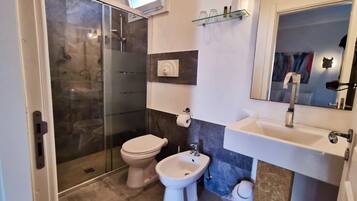 Ein Badezimmer mit Duschkabine aus Glas, Toilette, Bidet und Waschbecken mit Spiegel.