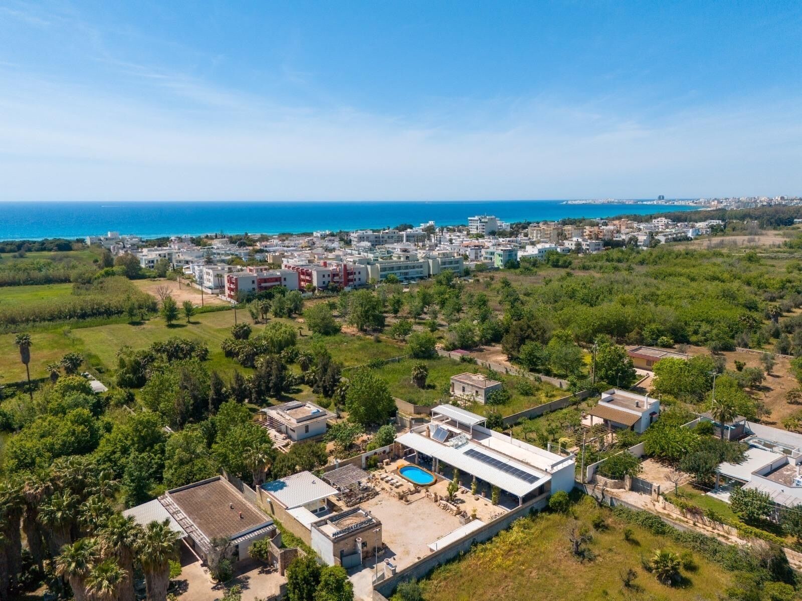 An aerial view of a coastal residential area with modern buildings, a swimming pool, and a clear view of the sea.