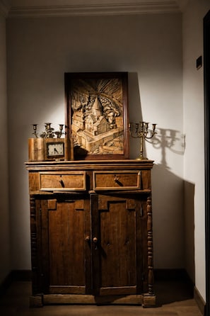 A wooden cabinet with a clock and candle holders, set against a wall with a framed artwork.
