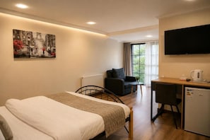 A hotel room with a bed, a desk, a chair, a television, and a painting on the wall.