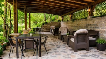 Un patio al aire libre con suelo de piedra, mobiliario de mimbre y una pérgola de madera.