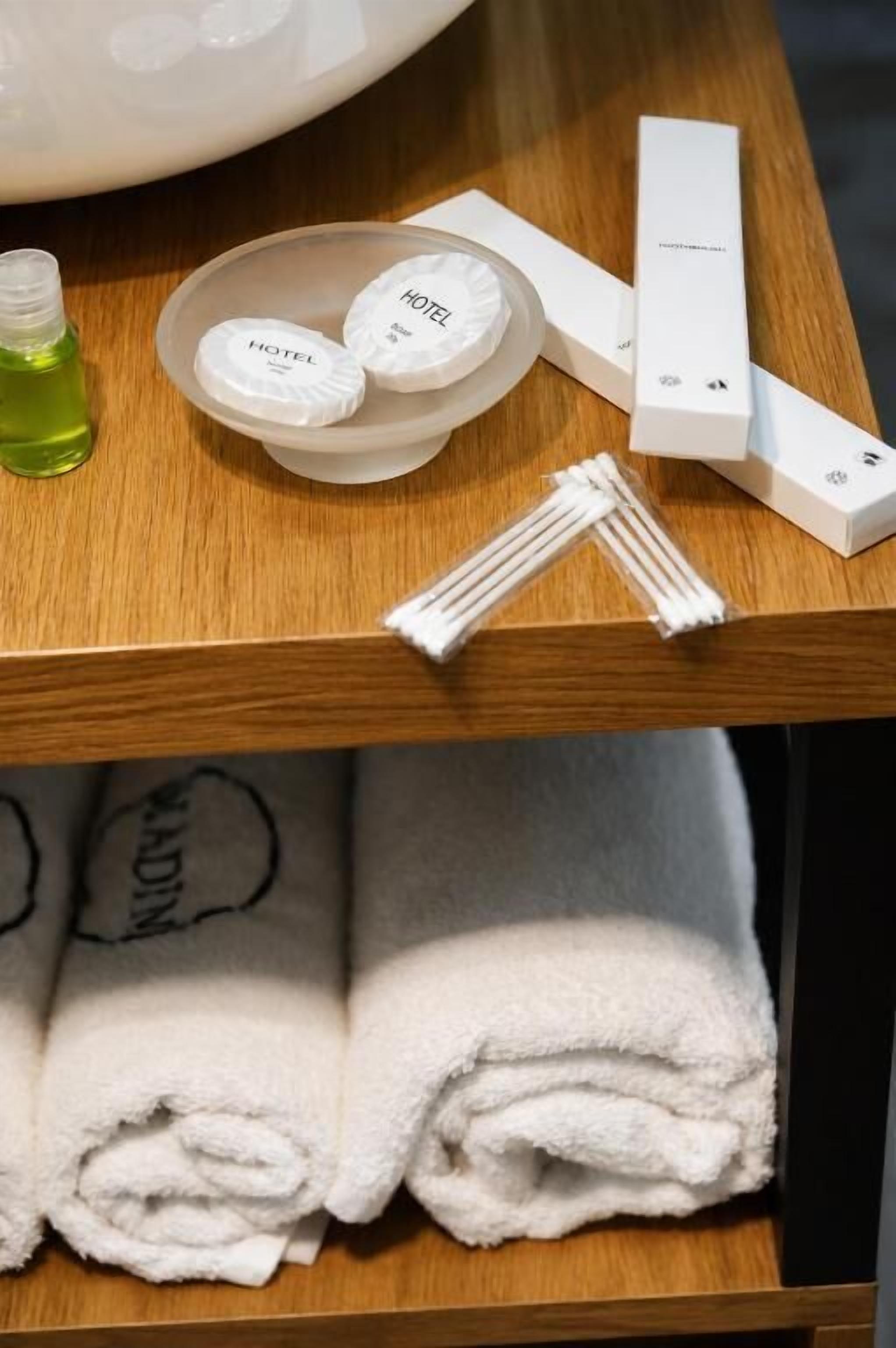 A hotel room with a wooden table displaying toiletries, a bottle of liquid soap, and neatly folded towels.